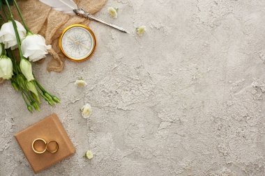 altın pusula, dağınık çiçekler, hediye kutusu ve gri dokulu yüzeyüzerinde beyaz eustoma çiçekler üzerinde altın yüzük yakın bej çuval bezi üzerinde quill kalem üst görünümü