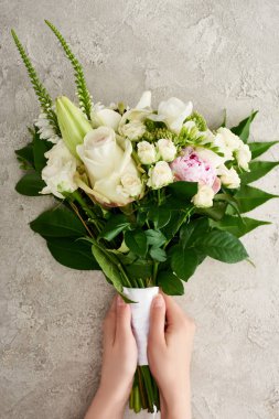 gri dokulu yüzeyde çiçek buketi tutan kadının kırpılmış görünümü