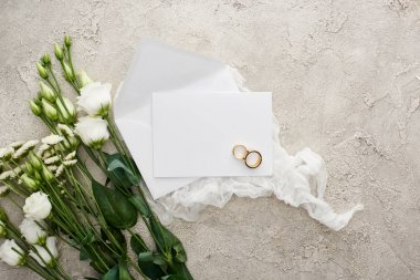 dokulu yüzeyde çiçeklerin yanında beyaz peynir bezi üzerinde boş kart üzerinde alyans üst görünümü