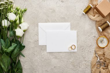 boş kart, eustoma çiçekler, hediye kutusu, pusula, makas ve dokulu yüzeyüzerinde bej çuval bezi üzerinde bobinler üzerinde alyans çifti üst görünümü 