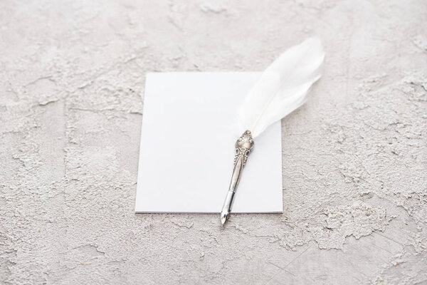 quill pen on white empty card on grey textured surface