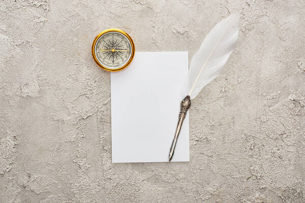 top view of quill pen on white card near golden compass on grey textured surface