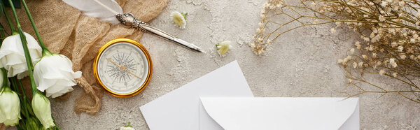 panoramic shot of quill pen on beige sackcloth near white envelope, golden compass and white flowers on grey textured surface 