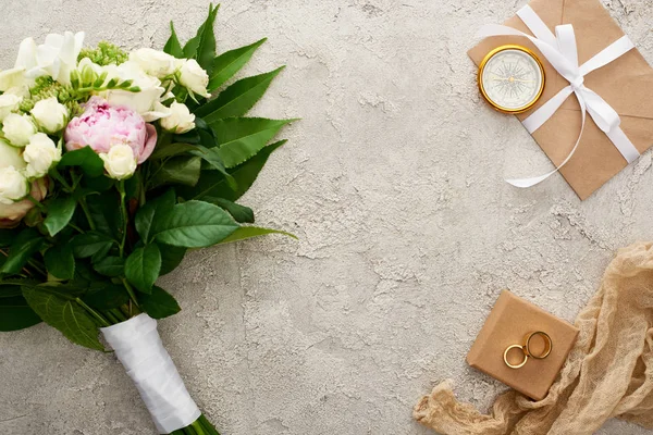 金色指南针 米色麻布 礼品盒上的结婚戒指和信封的顶视图 带白色丝带 靠近纹理表面的花束 — 图库照片