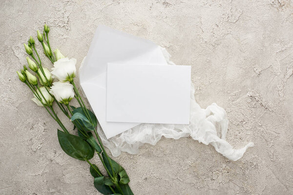 top view of blank white card on white cheesecloth near eustoma flowers on textured surface