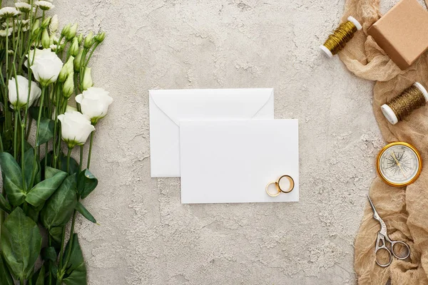 空卡上的一对结婚戒指 欧斯图玛花 礼品盒 指南针 剪刀和在纹理表面上的米色麻布上的线轴的顶视图 — 图库照片