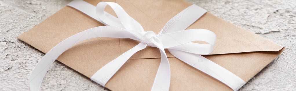 panoramic shot of beige paper envelope with white ribbon on textured surface