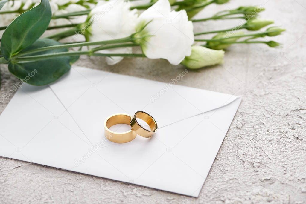 golden wedding rings on envelope near white eustoma flowers on textured surface 