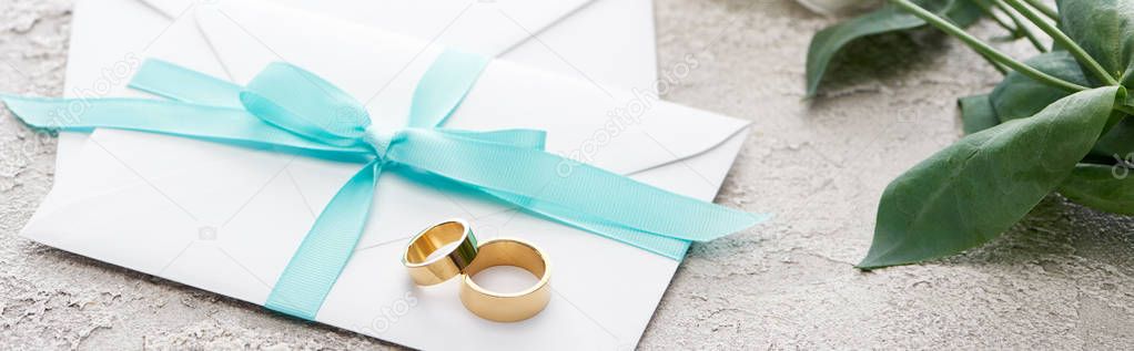 panoramic shot of golden rings on white envelopes with blue ribbon on textured surface