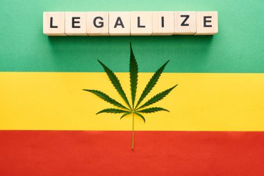top view of cannabis leaf and wooden blocks with legalize lettering on Rastafarian flag background clipart