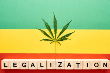 top view of cannabis leaf and wooden blocks with legalization lettering on Rastafarian flag background clipart