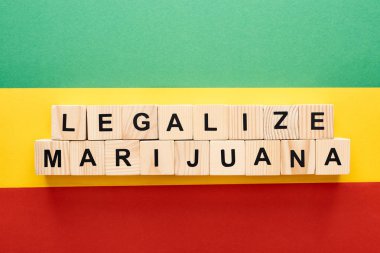 top view of wooden blocks with legalize marijuana lettering on Rastafarian flag background clipart