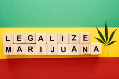 top view of cannabis leaf and wooden blocks with legalize marijuana lettering on Rastafarian flag clipart