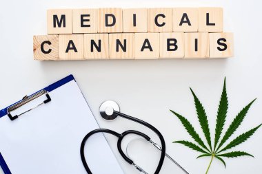 stetoskop yakınında marihuana yaprağı üst görünümü, beyaz arka plan üzerinde tıbbi esrar yazı ve pano ile ahşap bloklar