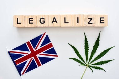 top view of green cannabis leaf and legalize lettering on wooden cubes near flag of Great Britain on white background clipart