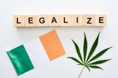 top view of green cannabis leaf and legalize lettering on wooden cubes near flag of Ireland on white background clipart
