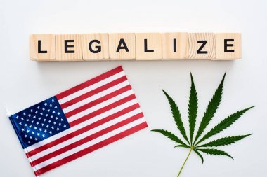 top view of green cannabis leaf and legalize lettering on wooden cubes near flag of America on white background clipart