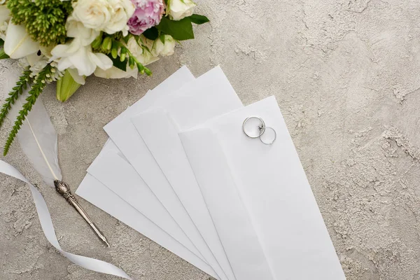 在纹理表面的信封上 靠近笔 白色丝带和花束的信封上看结婚戒指的顶视图 — 图库照片