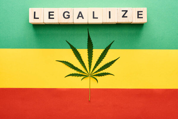 top view of cannabis leaf and wooden blocks with legalize lettering on Rastafarian flag background
