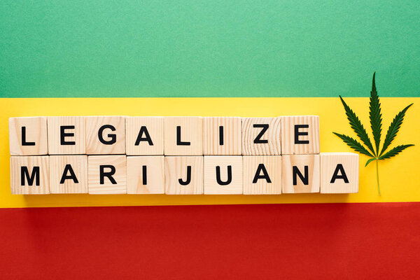 top view of cannabis leaf and wooden blocks with legalize marijuana lettering on Rastafarian flag