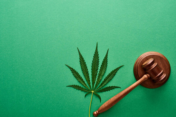 top view of green cannabis leaf with wooden gavel on green background