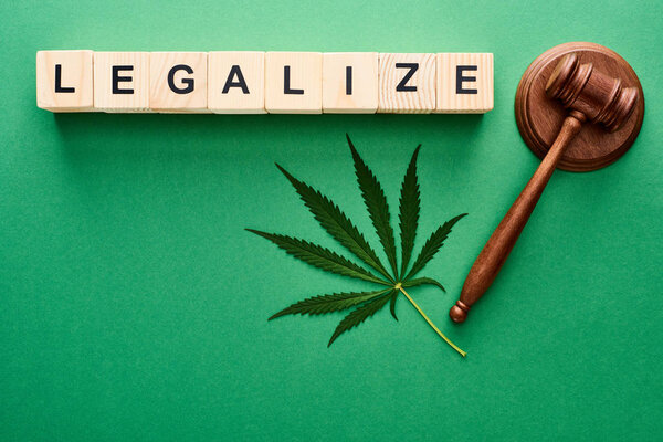 top view of green cannabis leaf, legalize lettering on wooden blocks and gavel on green background