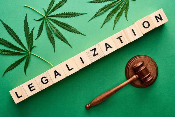 top view of green cannabis leaves and legalization word on wooden blocks near gavel on green background