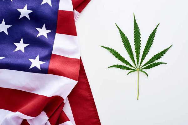 top view of green cannabis leaf near crumpled american flag on white background