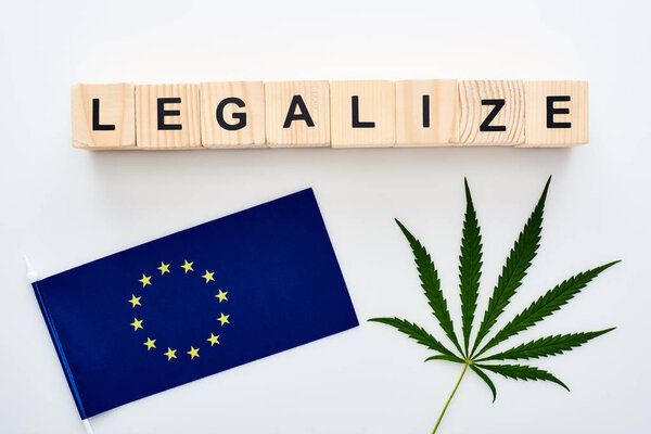 top view of green cannabis leaf and legalize lettering on wooden cubes near flag of Europe on white background