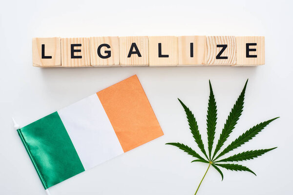 top view of green cannabis leaf and legalize lettering on wooden cubes near flag of Ireland on white background