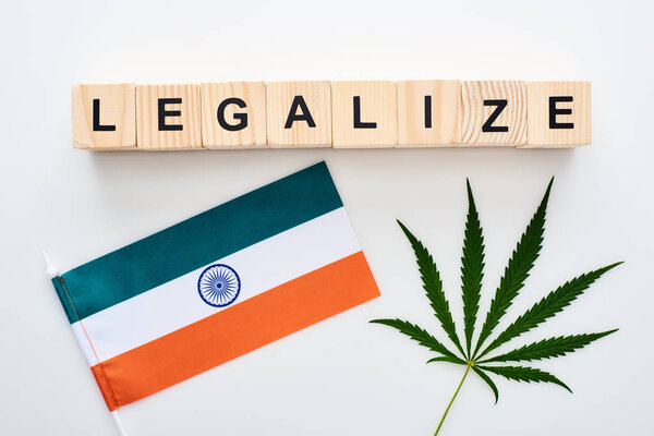 top view of green cannabis leaf and legalize lettering on wooden cubes near flag of India on white background