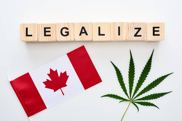 top view of green cannabis leaf and legalize lettering on wooden cubes near flag of Canada on white background