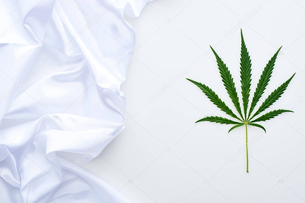 top view of green cannabis leaf near white flag on white background