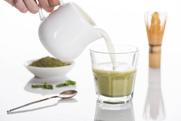 cropped view of woman pouring milk into matcha matcha tea on table with whisk and powder 