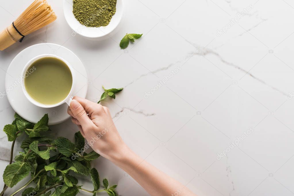 top view of woman holding matcha matcha tea on table with whisk, powder and mint 
