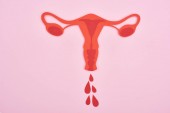 Ansicht von rotem Papier geschnitten weibliche Fortpflanzungsorgane mit Bluttropfen auf rosa Hintergrund 