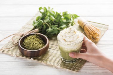 çırpma, toz ve nane ile masada krem şanti ile matcha matcha çay tutan kadın kırpılmış görünümü 