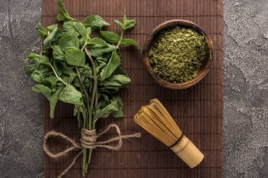 koyu taş masa üzerinde bambu mat üzerinde yeşil matcha çay tozu, nane ve çırpma üst görünümü