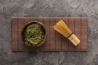 koyu taş masa üzerinde bambu mat üzerinde çırpma teli ile matcha çay tozu üst görünümü