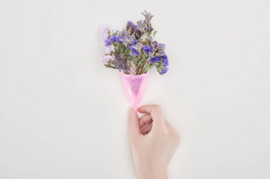 gri izole kır çiçekleri ile pembe plastik adet fincan tutan kadının kısmi görünümü