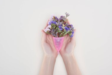 cropped view of woman holding menstrual cup with wildflowers isolated on grey clipart