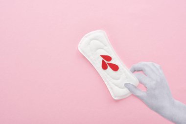 cropped view of hand holding white sanitary napkin with blood drops on pink background clipart