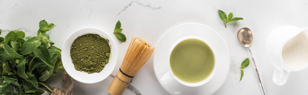 На белом столе лежат зеленый чай маття, мята и молоко
