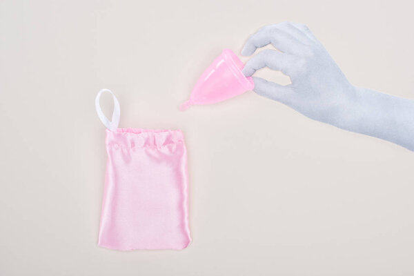 top view of white paper hand holding pink plastic menstrual cup near bag isolated on grey