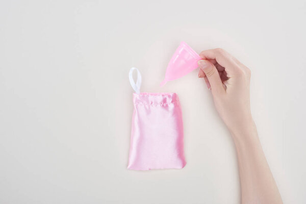 cropped view of woman holding pink plastic menstrual cup near bag isolated on grey
