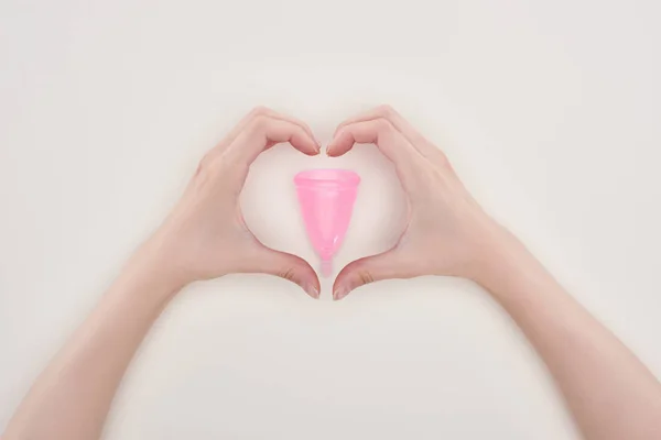 裁剪视图的妇女显示心脏标志与手周围的粉红色塑料月经杯隔离在灰色 — 图库照片