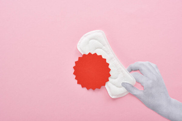 cropped view of hand holding white sanitary napkin with blood sign on pink background