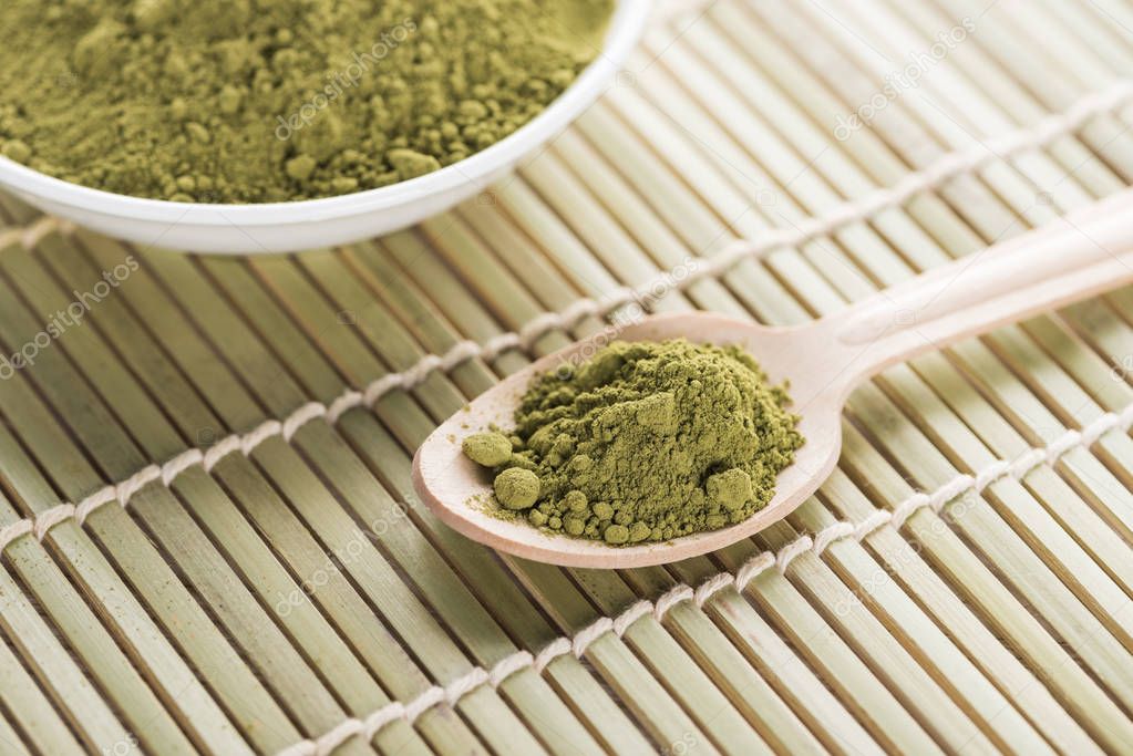 bowl and wooden spoon with powder of green matcha tea on bamboo mat