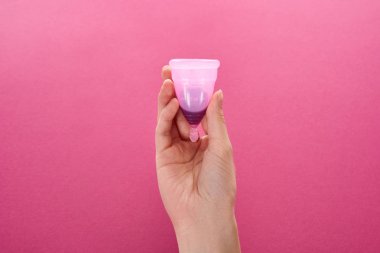 partial view of woman holding menstrual cup with blood on purple background clipart