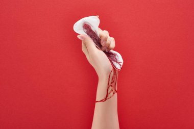 partial view of woman squeezing sanitary towel with blood on red background clipart